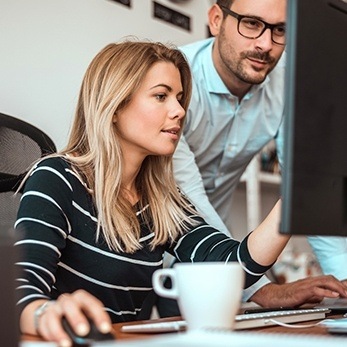 one woman and one man looking at a computer monitor