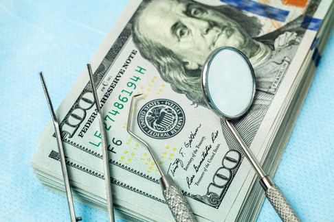 A stack of hundred dollar bills with dental instruments placed on top